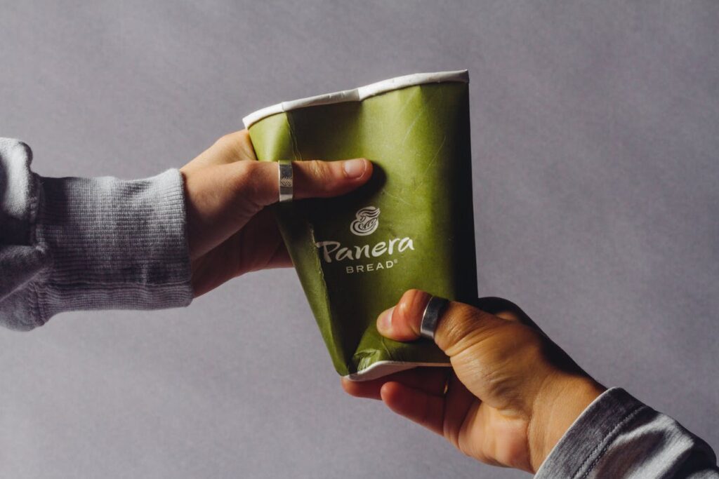 una persona aplastando un vaso de panera bread con las manos