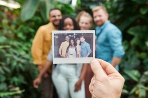 un grupo de amigos en segundo plano. En primer plano, la foto polaroid que les acaban de sacar sostenida por una mano